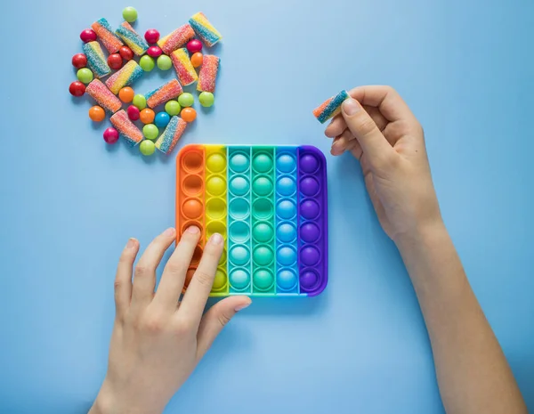 Çocuk gökkuşağı Pop ile oynuyor renkli cereyan ve kalp şeklinde marmelatların yanında oyuncak kıpırdıyor. Patlat - mavi arka plandaki çocuklar için yeni bir stres önleyici oyuncak.