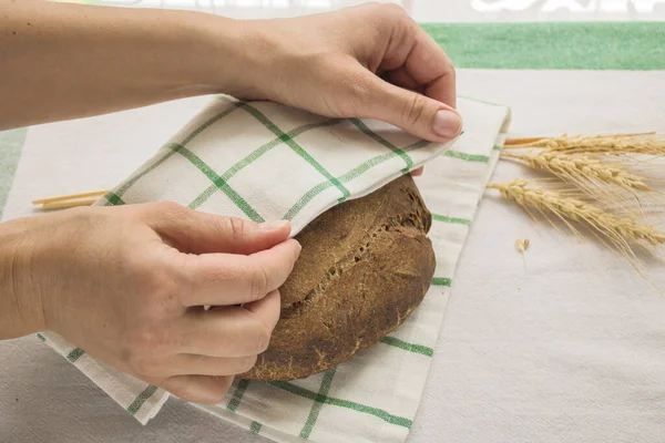 Women\'s hands cover a freshly backed round bread by linen napkin next to the ears of grain. Homemade organic bread. Photo with step by step recipe