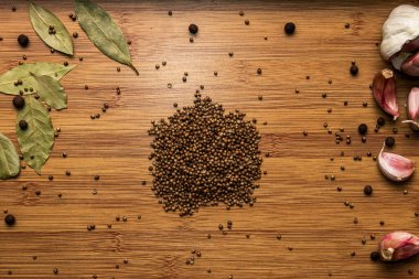 Tahta bir arka planda kişniş tohumu. Yukarıdan bak. Arka planda sarımsak ve defne yaprağı var. Et ve çay mevsimleri..