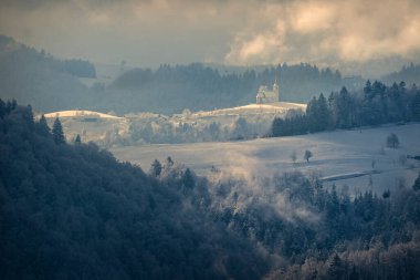 Öğleden sonra güneşiyle aydınlatılmış, güzel, eski bir kilisenin olduğu kış manzarası. İnancın sembolü olarak Katolik tapınağı.