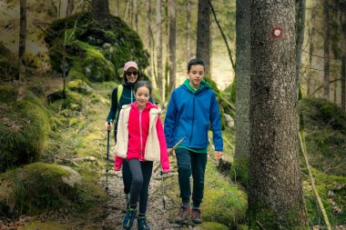 Anne kız ve oğluyla ormanda yürüyüş yapıyor. Bahar başında aile aktivitesi. Ceketlerle işaretlenmiş iz.