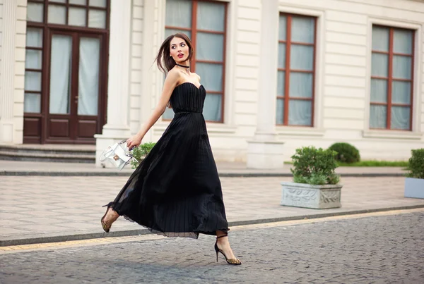 Ομορφότερη μόδας νεαρή γυναίκα στο μακρύ φόρεμα που τρέχει με τσάντα. — Φωτογραφία Αρχείου