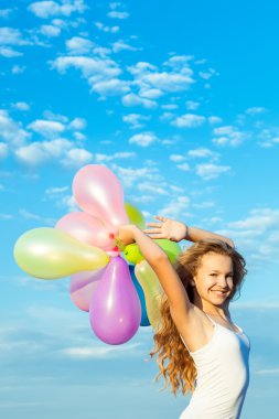 Mavi gökyüzünde renkli balonlar tutan mutlu kız