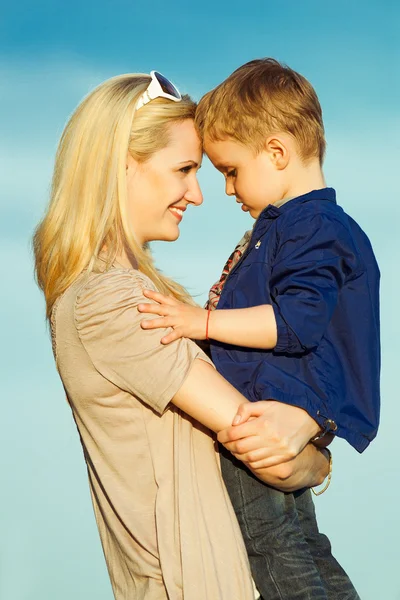 Happy mother and child son hugging and smiling over blue sky at — Stock Photo, Image