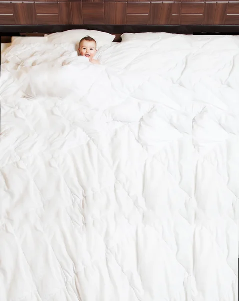 ファニーとかわいい赤ちゃんが大きめのベッドで毛布の下で笑っています。コピー スパ — ストック写真