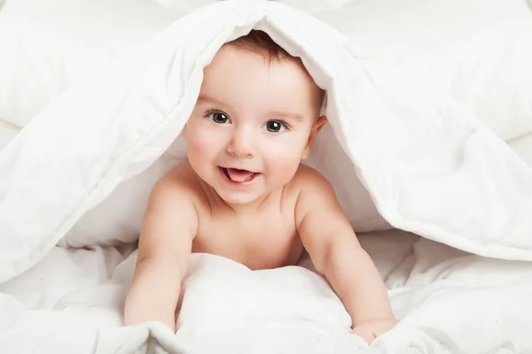 Lustiges und süßes kleines Baby, das unter weißer Decke lächelt. — Stockfoto
