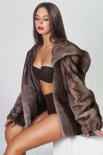 Glamour hermosa mujer en abrigo de visón de piel sentado en cubo sobre wh —  Fotos de Stock
