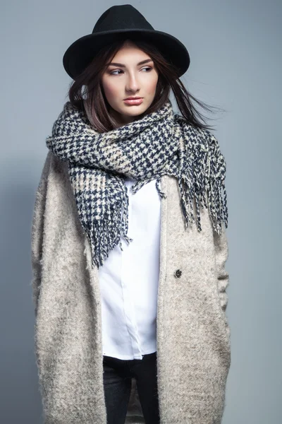 Модна жінка в пальто, вовняний шарф і капелюх позує в студії на сірому фоні . — стокове фото