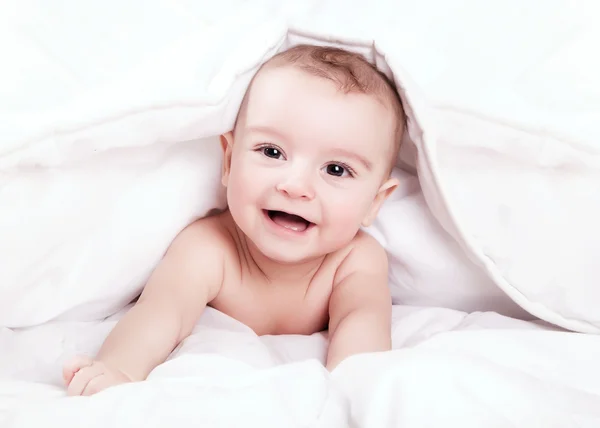 Beyaz örtünün altında gülümseyen mutlu ve sevimli küçük bebek. — Stok fotoğraf