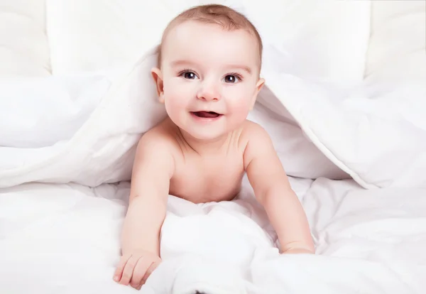 Милый и забавный малыш улыбается под белым одеялом. Copy spa — стоковое фото