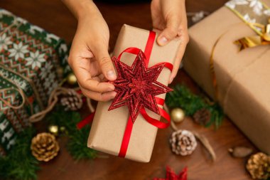 Noel hediyesi tutan bir kadının elleri. Hediyenin kırmızı bir kurdelesi ve yıldızı var.