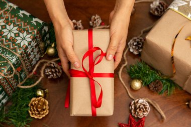Noel hediyesi tutan bir kadının elleri. Hediyenin kırmızı bir kurdelesi ve yıldızı var.
