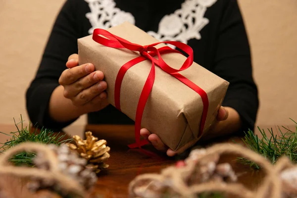 Noel hediyesi tutan bir kadının elleri. Hediyenin kırmızı bir kurdelesi ve yıldızı var.