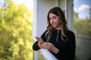 Genç bir kadın dışarıda tek başına duruyor ve cep telefonuna mesaj gönderiyor.