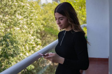 Genç bir kadın dışarıda tek başına duruyor ve cep telefonuna mesaj gönderiyor.