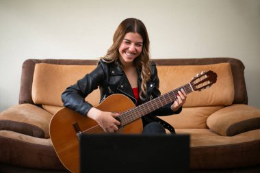 Kız oturma odasında akustik gitar çalıyor. Evde internetten ders alıyor.