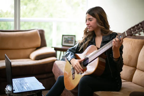Kız oturma odasında akustik gitar çalıyor. Evde internetten ders alıyor.