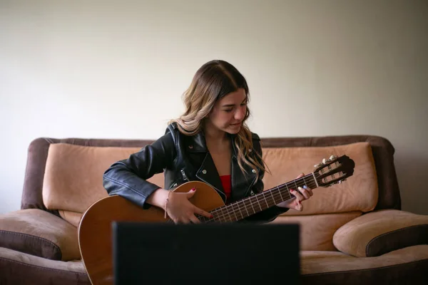 Kız oturma odasında akustik gitar çalıyor. Evde internetten ders alıyor.