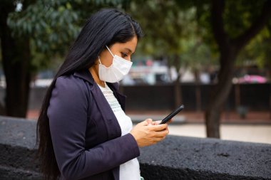 Maskeli bir iş kadını, telefonunda daktilo yazıyor.