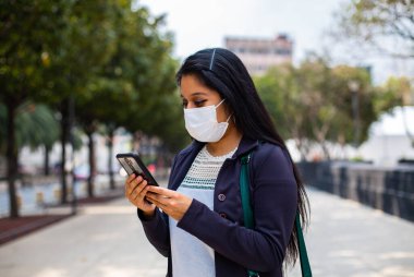 Maskeli bir iş kadını, telefonunda daktilo yazıyor.