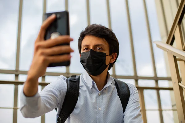 Maskeli genç adam, yemek merdivenlerinde oturuyor, telefonu elinde, selfie çekiyor.