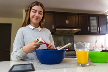 Genç kadın tabletiyle yemek yapmayı öğreniyor. O gülümsüyor. Mutfakta..