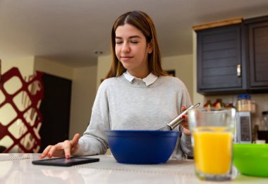 Genç kadın tabletiyle yemek yapmayı öğreniyor. O gülümsüyor. Mutfakta..