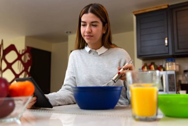 Genç kadın tabletiyle yemek yapmayı öğreniyor. O gülümsüyor. Mutfakta..