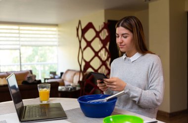 Genç kadın laptopuyla yemek yapmayı öğreniyor. O gülümsüyor. Mutfakta..
