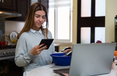 Genç kadın dijital tabletini kullanıyor. O gülümsüyor. Laptopuyla yemek yapmayı öğreniyor.