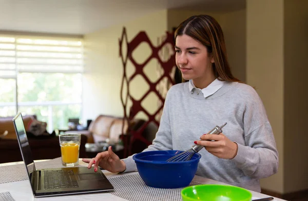 Genç kadın laptopuyla yemek yapmayı öğreniyor. O gülümsüyor. Mutfakta..