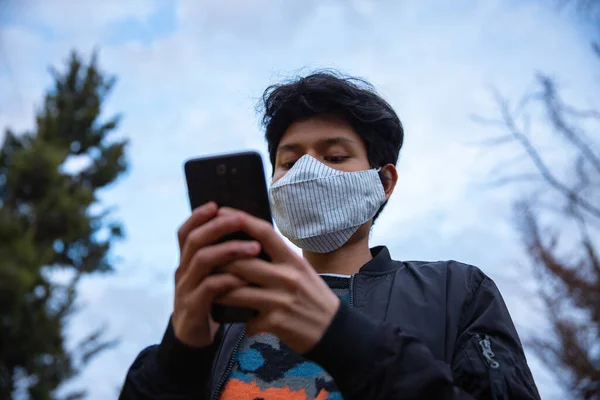 Maskeli genç latin adam sokakta telefonunu kullanıyor.