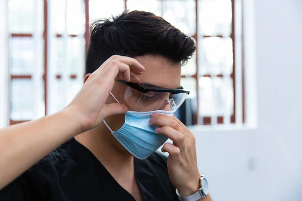 Close-up of a doctor with mask and glasses against there is a window and white background