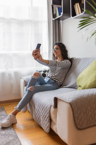 Oturma odasında gözlüklü genç kız telefonuyla selfie çekiyor..