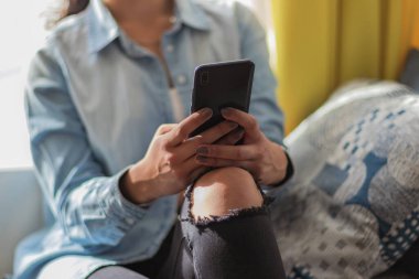 Kanepede oturan ve odasında akıllı telefon kullanan genç bir kadının fotoğrafını çek.