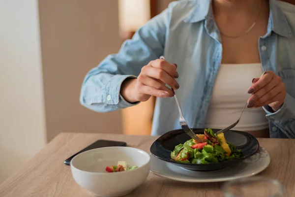 Genç esmer kadın yemek odasında salata yiyor..