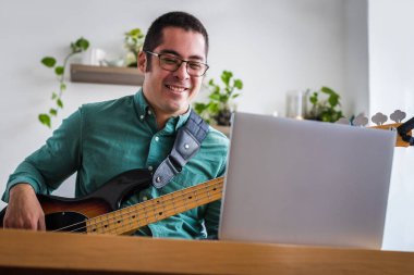 Genç adam dizüstü bilgisayarla masada oturuyor. Canlı müzik öğretiyor.