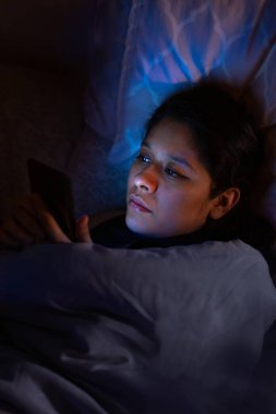 Genç bir kadının yatağında çekilmiş bir fotoğrafı. Telefonunu kullanıyor..