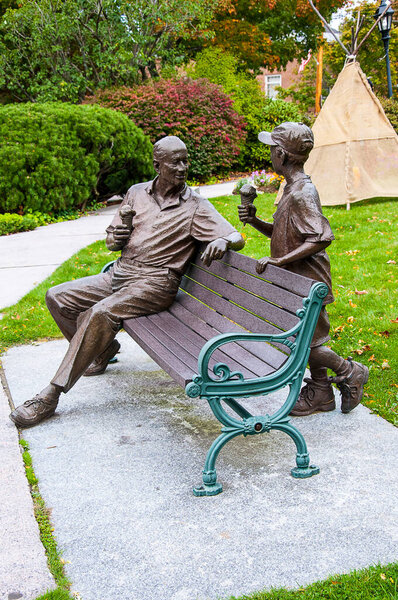 Wolfeboro on Lake Winnipassaukee in New Hampshire USA. Called 'Sharing' this bronze sculpture of a grandfather seated is enjoying a moment with his grandson.  Wolfeboro oldest summer resort in America. The work was created by sculptor Derek Wernher.