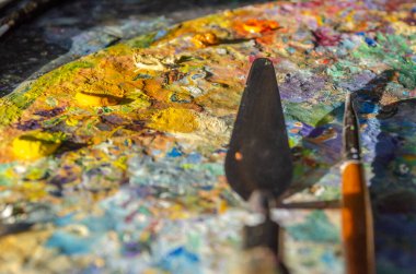 Bir ressamın palet üzerindeki fırça ve palet bıçağının güneş ışığıyla karışık ve karıştırılmamış yağlı renkleri.