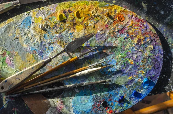 Stock Photo of a painter brushes and palette knife on a palette with mixed and unmixed oil colours with sunlight