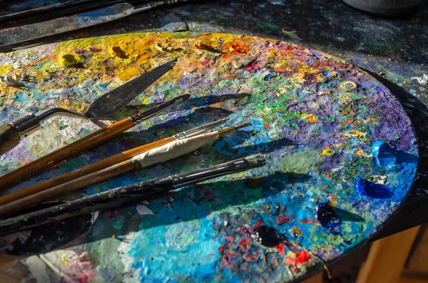 Stock Photo of a painter brushes and palette knife on a palette with mixed and unmixed oil colours with sunlight