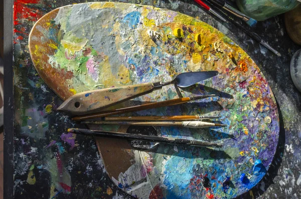 Stock Photo of a painter brushes and palette knife on a palette with mixed and unmixed oil colours with sunlight