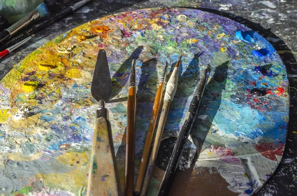 Stock Photo of a painter brushes and palette knife on a palette with mixed and unmixed oil colours with sunlight