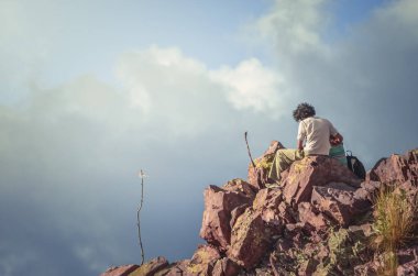 Tanınmayan bir adam ve kadın gökyüzü ve bulutlarla bir dağda oturuyorlar. Tepeler ve dağlar manzaralı. Iruya, Salta, Arjantin