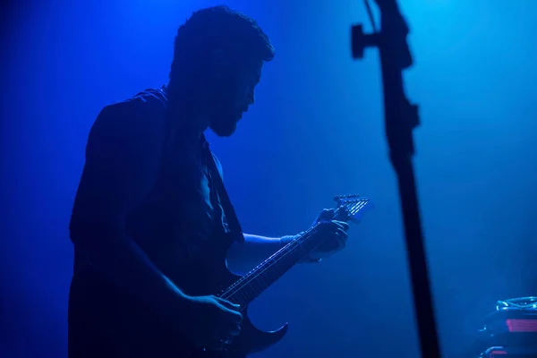 Rock grubu konserinde elektro gitar çalan müzisyen. Sahnede çalan siyah saçlı erkek gitarist. Müzik sisli ışıklar silueti gösterir