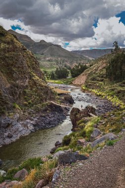 Colca Vadisi 'ndeki Colca Nehri üzerindeki küçük tahta köprüden geçen insanlar. Peru, Güney Amerika. Dağlar ve bulutlar