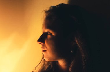 Geceleri uzun saçlı, güzel bir kadın. Karanlık bir odada. Spot lamba ışığında. Siyah arka plan ve sarı ışık. İçerideki portre.