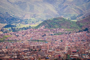 Altında yeşil tarlalar ve tepelerle çevrili Cusco şehrinin çatılarının havadan görüntüsü. Uzak bir noktadan evler ve kiliseler. Peru, Güney Amerika