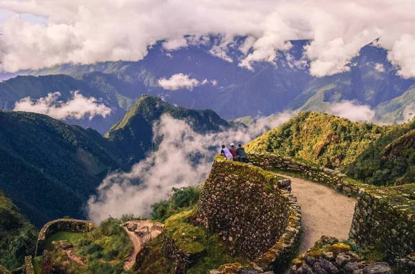 Phuyupatamarca harabelerinde önlerindeki büyük vadiyi düşünen üç sırt çantalı erkek arkadaşın yüksek açılı görüntüsü. Peru 'daki Machu Picchu' ya giden İnka yolu. Güney Amerika